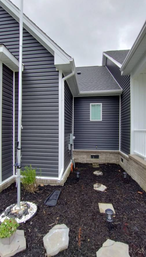 Seamless gutter and white downspout installed along dark siding